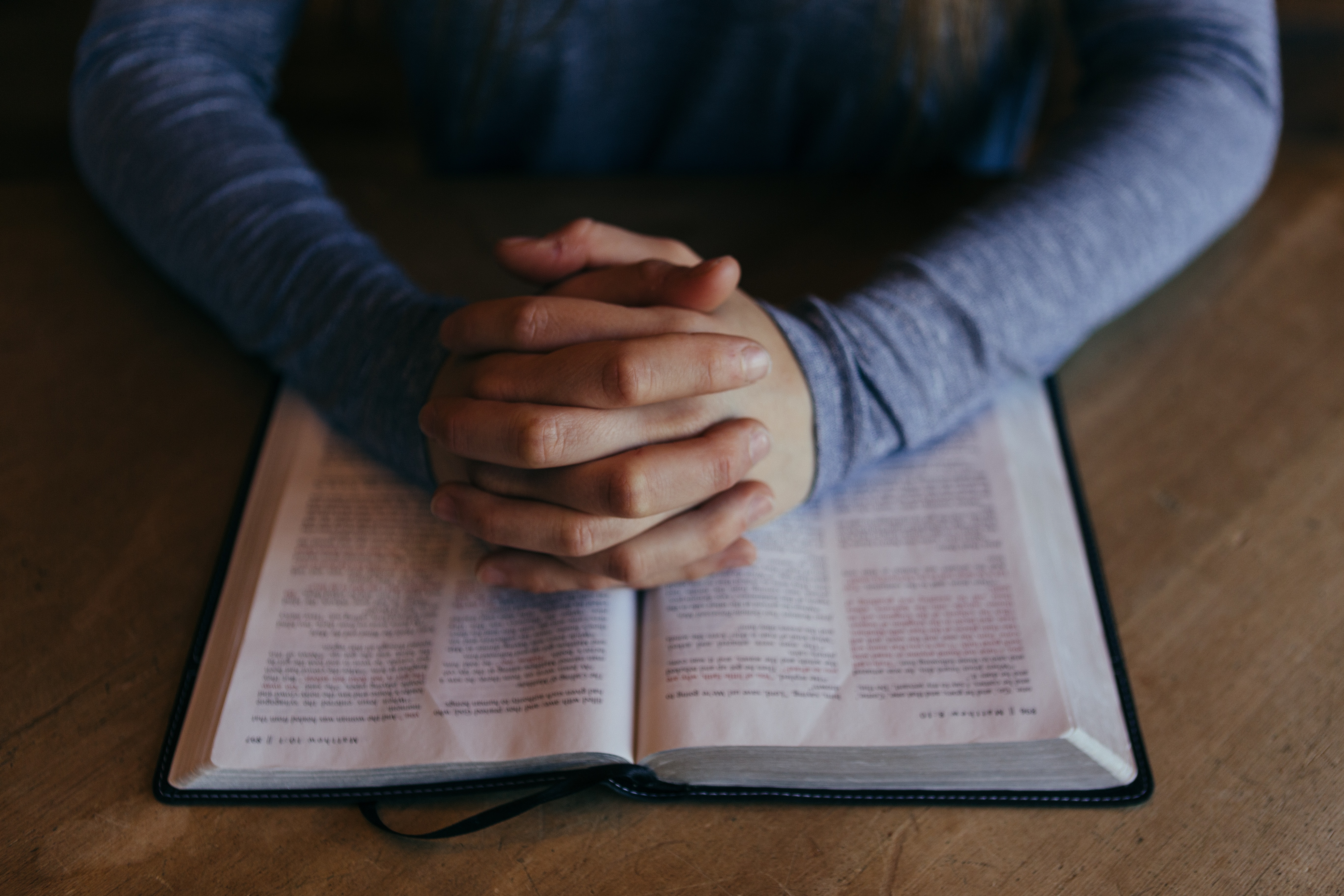 Hands folded in prayer over an open Bible